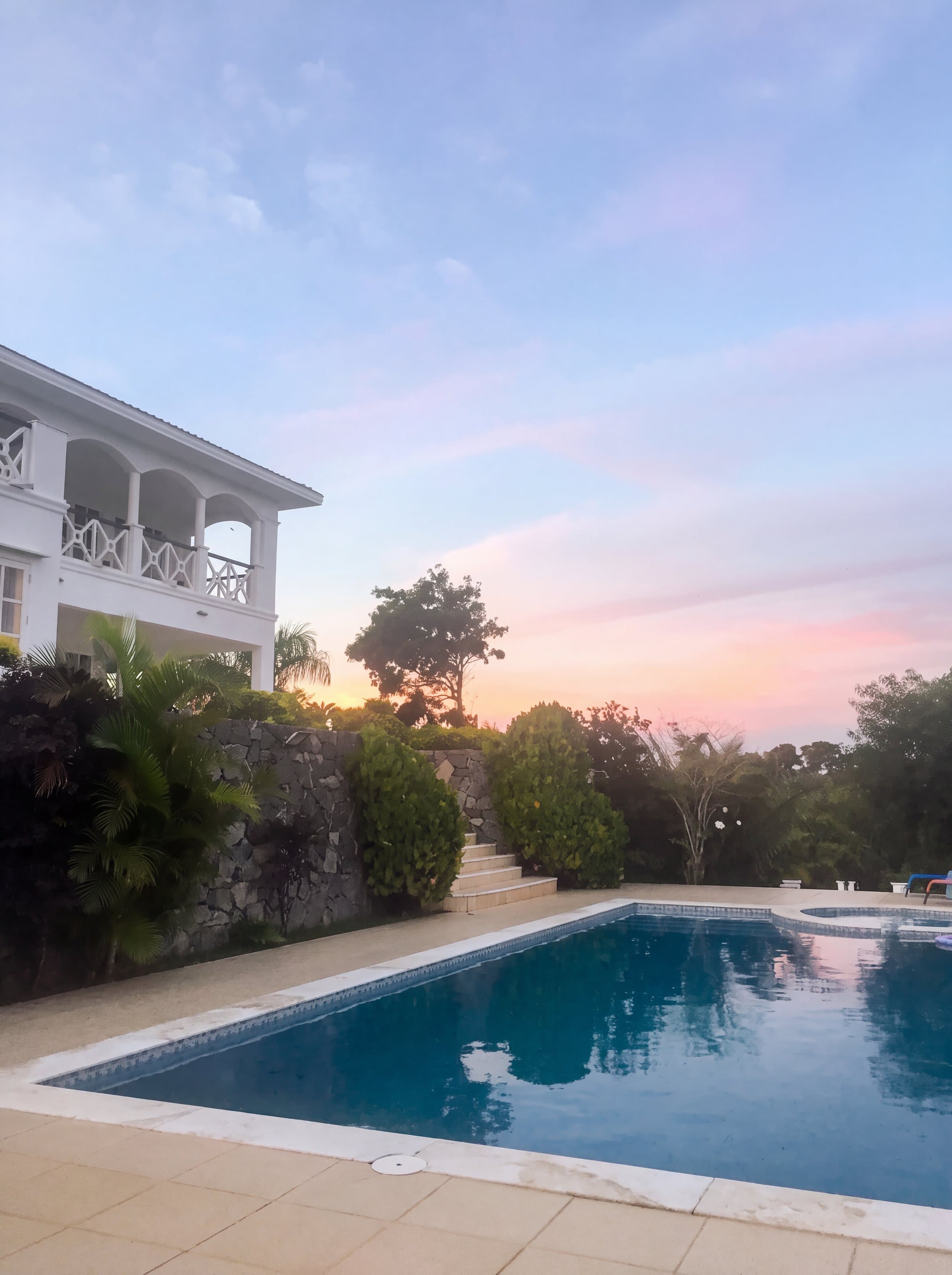 Varanda em arcos e piscina ao entardecer, com céu rosado