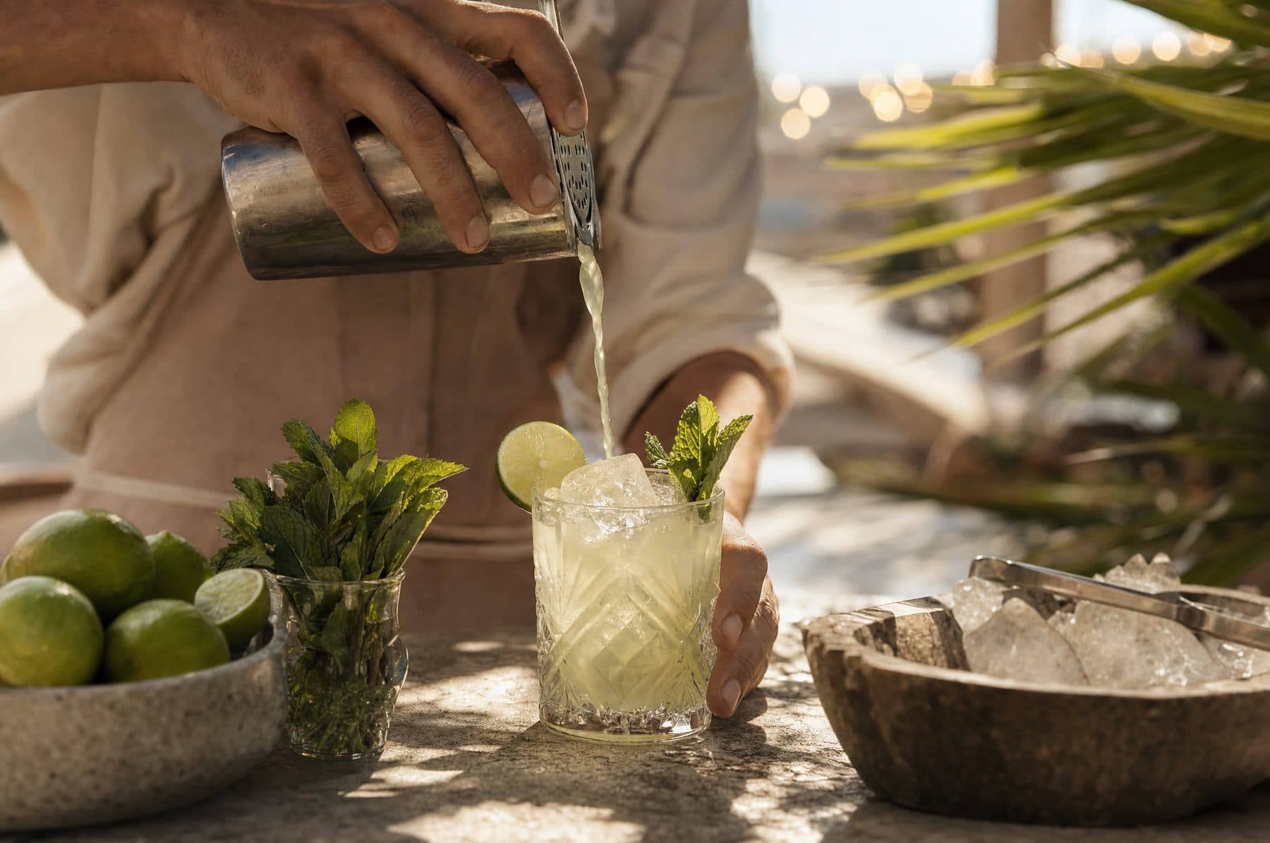 Imagem ilustrativa: mãos de um barman servindo um drinque cítrico em balcão ao ar livre