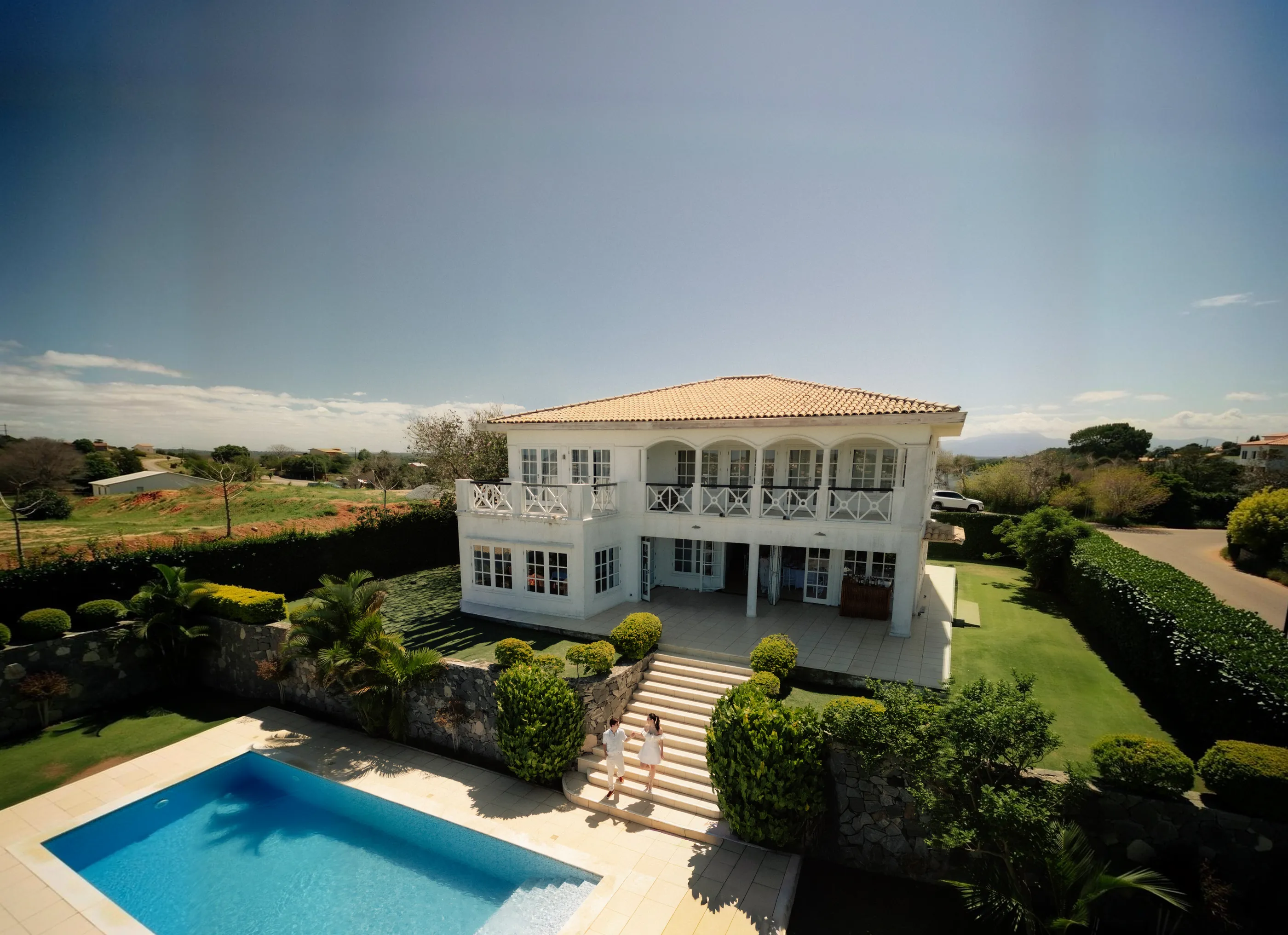 Vista aérea da casa com um casal vestido de branco descendo a escadaria
