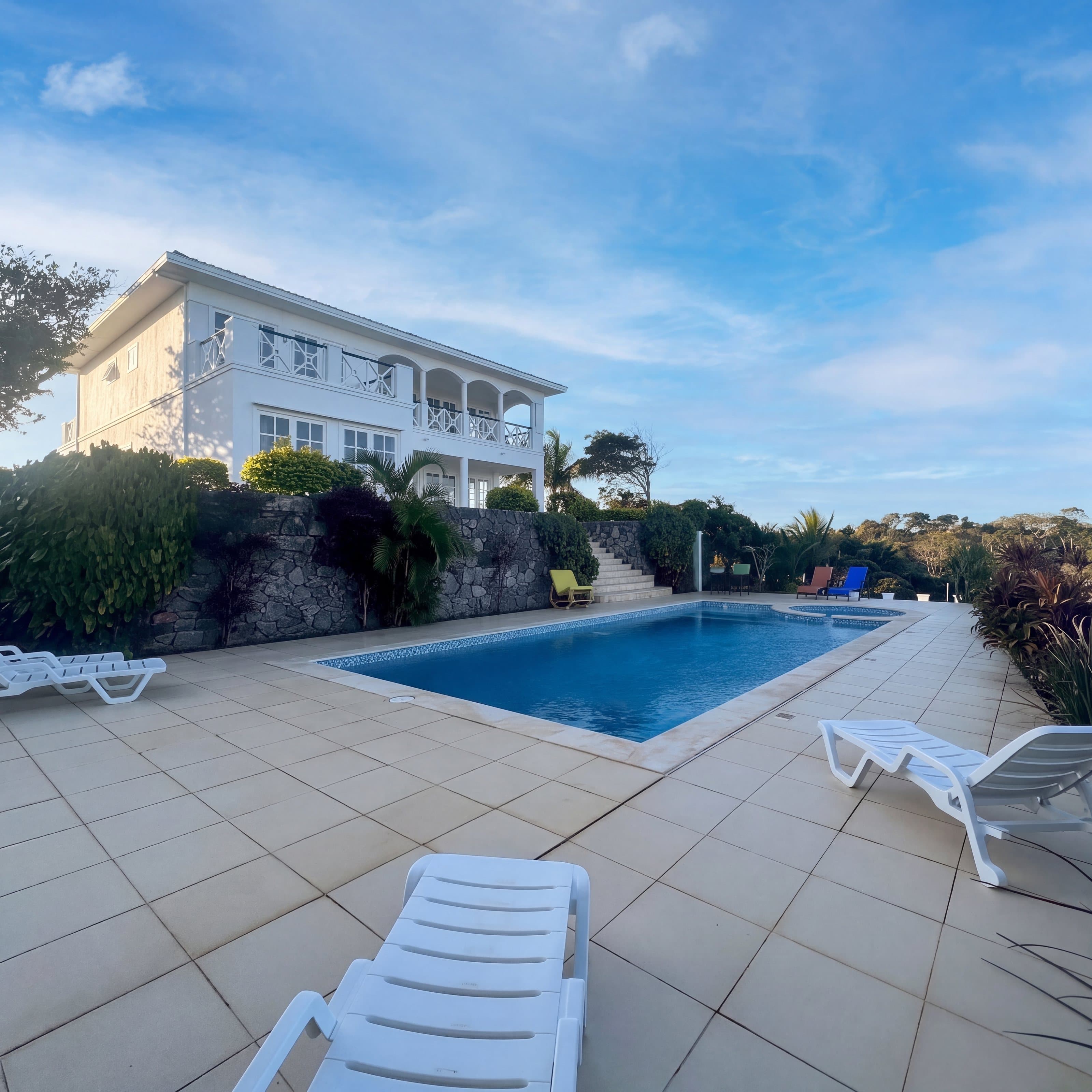 Deck da piscina com espreguiçadeiras brancas e a casa ao fundo, no fim da tarde